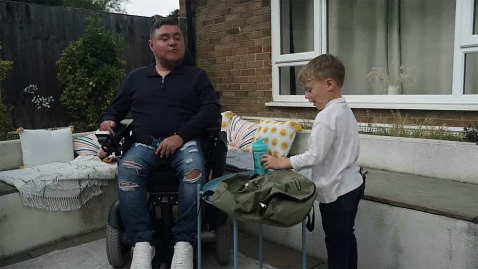 A man in a wheelchair and a young boy organizing items outdoors, symbolizing responsible cannabis packaging that prioritizes accessibility and family safety.